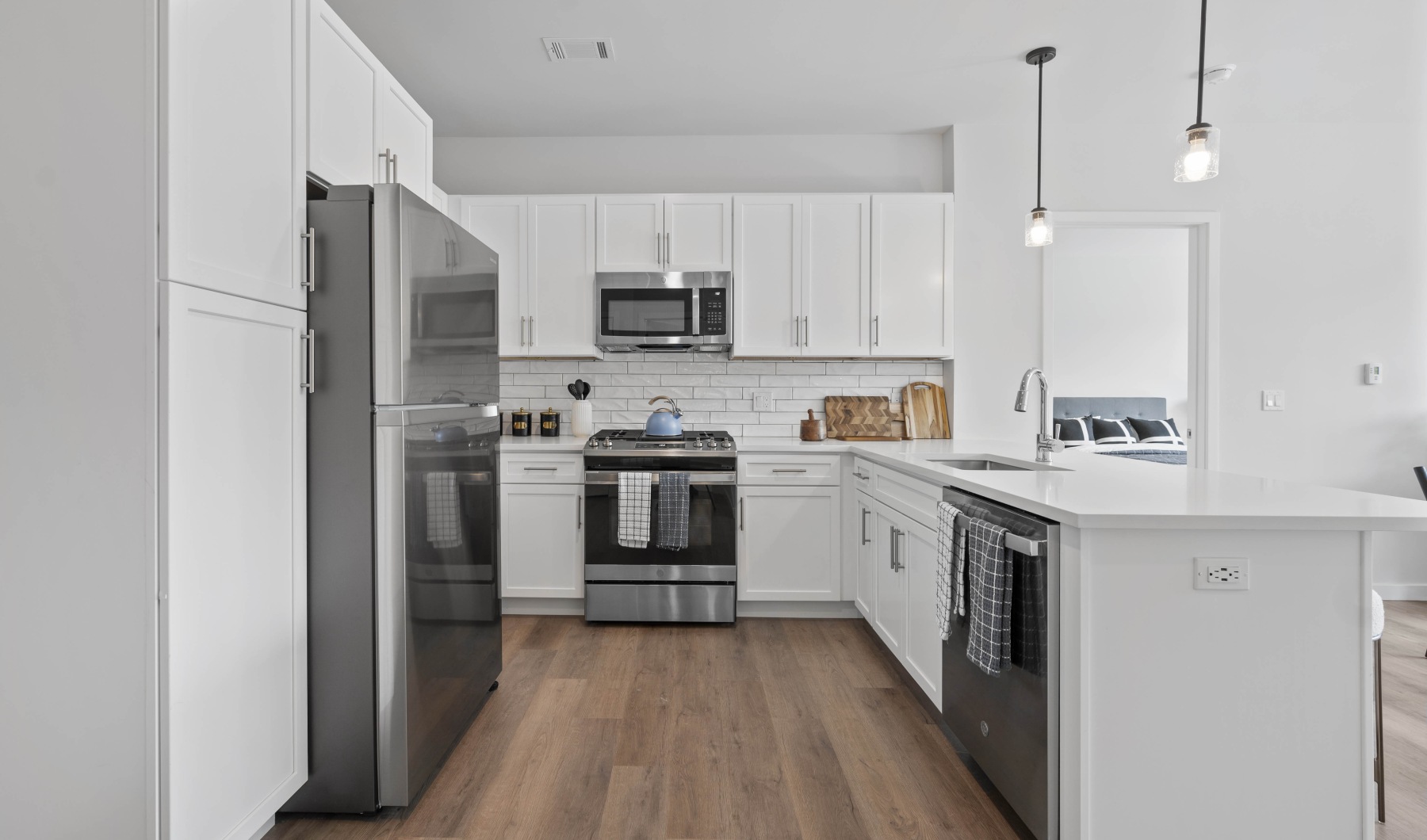 Luxury apartment kitchen with white cabinetry, white tile backsplash, kitchen island, stainless steel appliances, and wood like flooring 