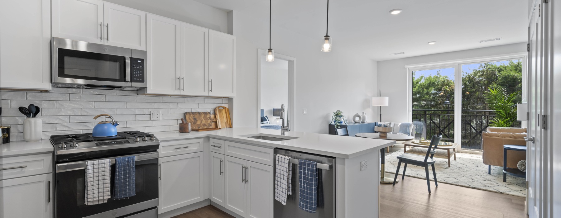 Model kitchen and living room at our apartments for rent in Wilton, CT featuring wood grain floor paneling and a view of lush greenery outside apartment