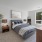 Spacious bedroom with bed, two side tables, plant, mirror, and oversized windows with natural light
