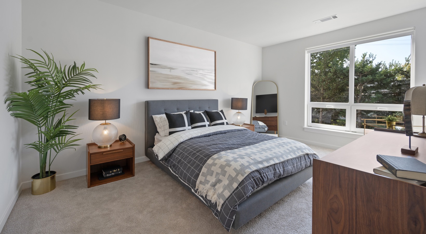 Spacious Bedrooms Spacious bedroom with bed, two side tables, plant, mirror, and oversized windows with natural light