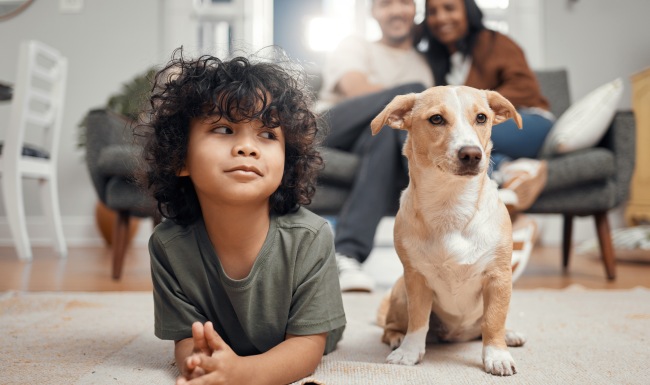 Pet friendly community Child next to dog in apartment with parents in the background on a couch